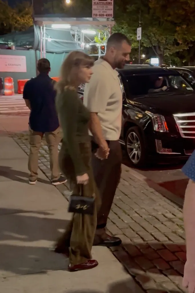 Taylor Swift and Travis Kelce hold hands while walking down a New York City sidewalk at night.