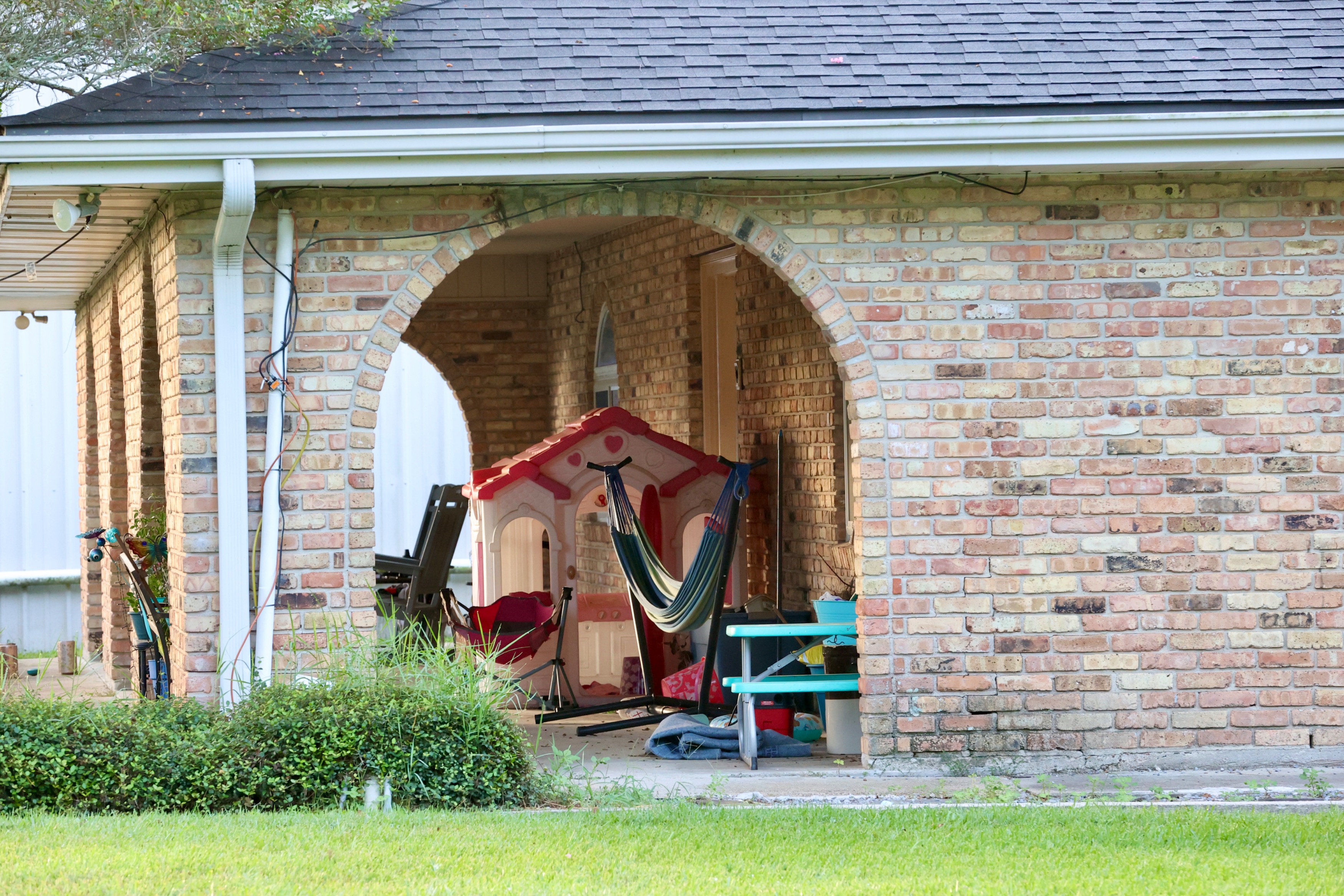 Exterior view of the brick home of Ken Urker, featuring a covered patio with outdoor toys and a hammock.
