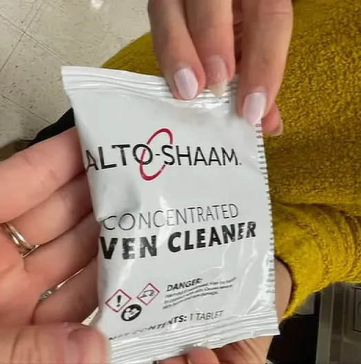 A person holding a packet of Alto-Shaam concentrated oven cleaner.