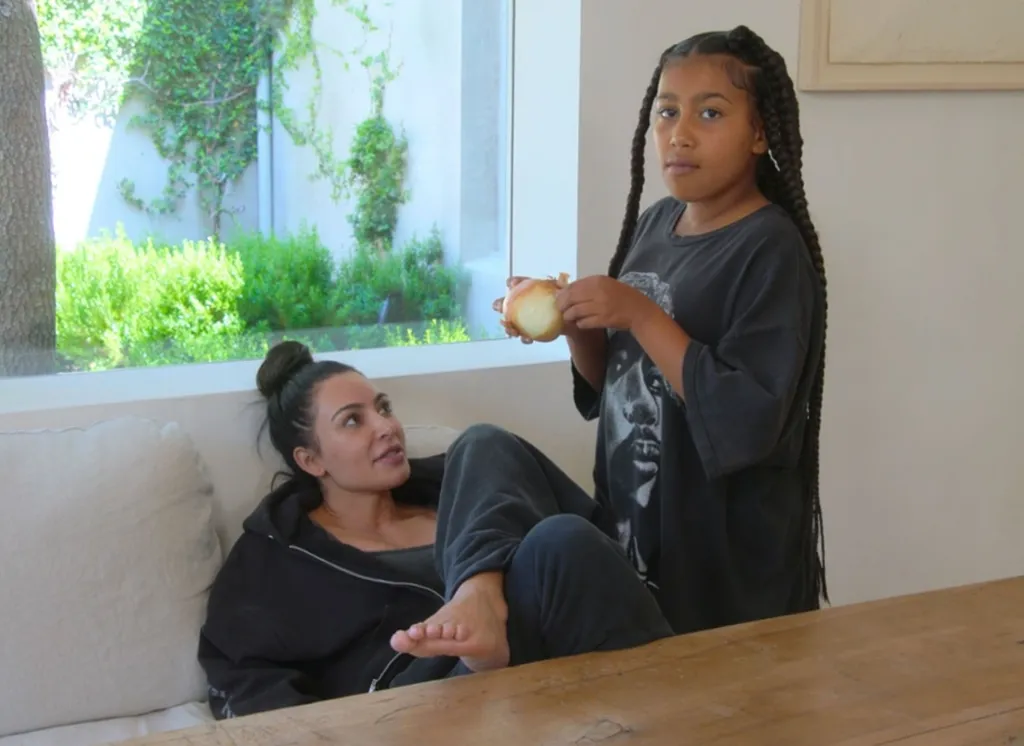 Kim Kardashian relaxing on a couch while her daughter North West holds a raw onion.