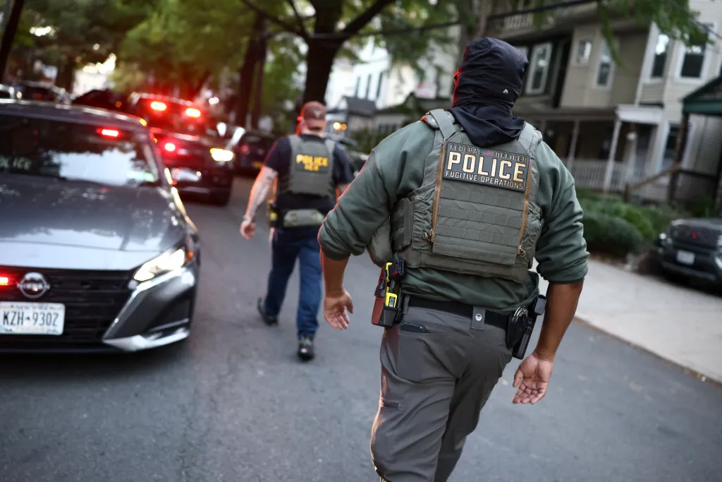 Federal agents in tactical gear walk near the scene of an ICE operation in New York.