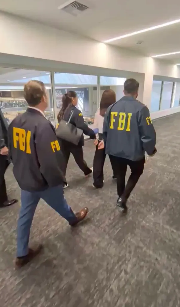 Wanying Zhang is escorted by FBI agents down an airport corridor.