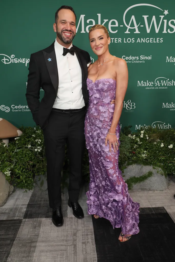Bill Fishel and guest pose in front of a branded green backdrop at the Make-A-Wish Foundation Gala.