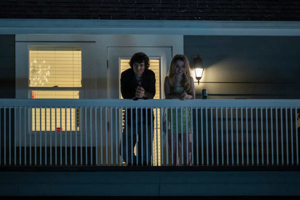 Arthur Conti and Alison Thornton standing on a porch at night, leaning on a white railing in a scene from 