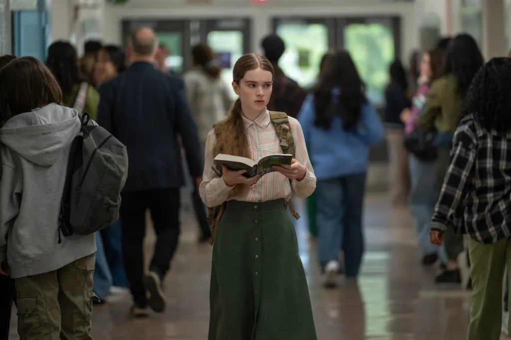 Summer H. Howell stands in a crowded school hallway, reading a book.