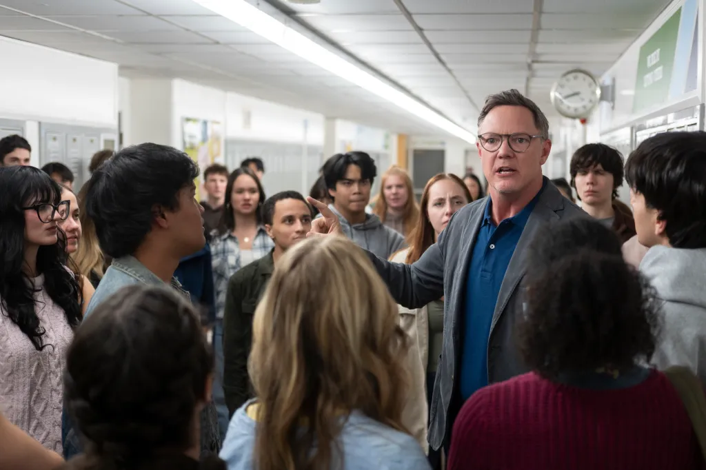 Matthew Lillard in a scene from Carrie, pointing a finger in a crowded high school hallway.