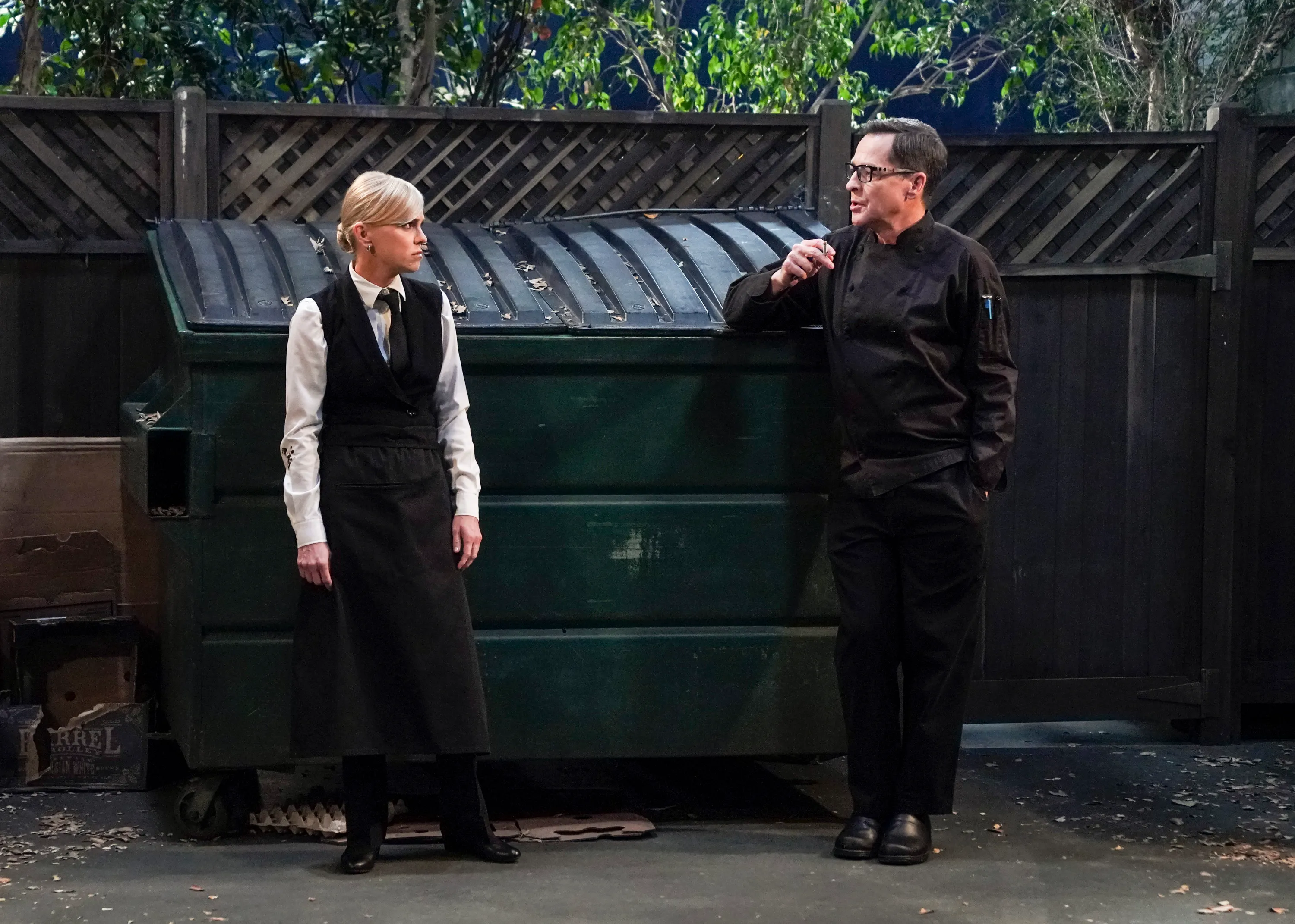 Christy and Chef Rudy talking in an alleyway next to a dumpster.