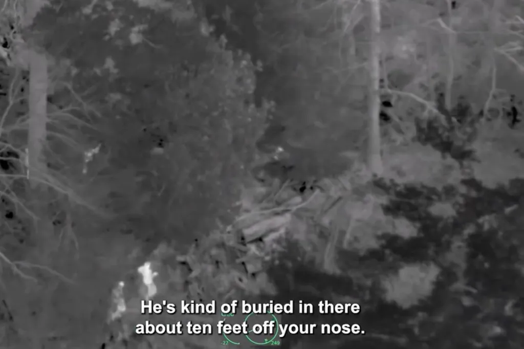 Forward-looking infrared (FLIR) camera view showing an escaped inmate hiding under logs and debris in the woods.