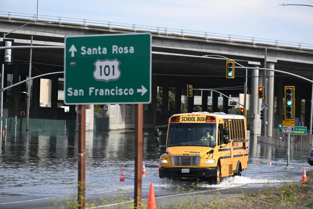 A yellow school bus drives through floodwaters on a road in Mill Valley, Marin County, California.