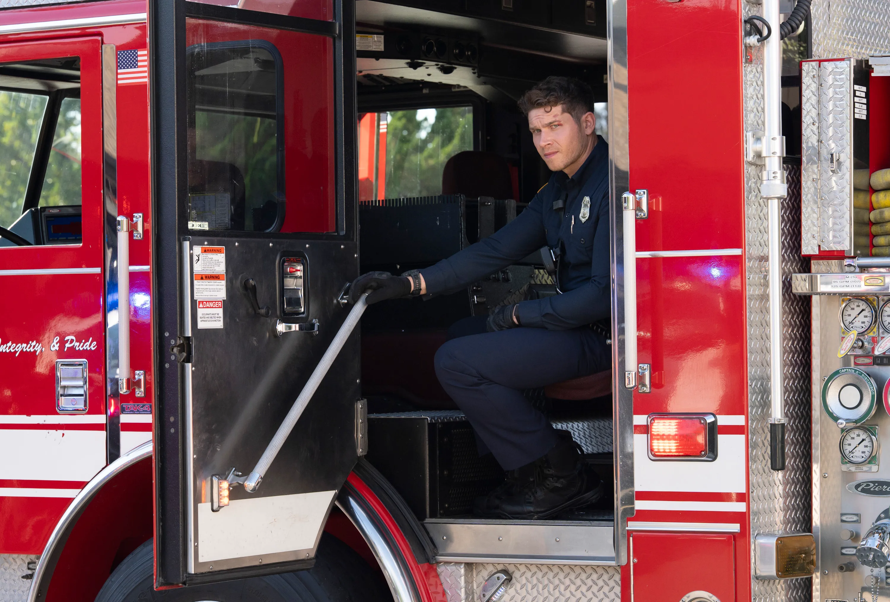 Actor Oliver Stark as firefighter Chimney sitting in the open door of a fire truck.