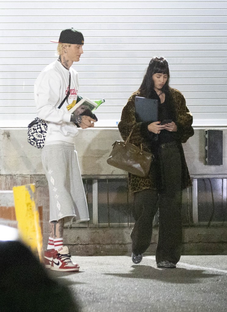 Machine Gun Kelly and Dakota Johnson walking together outside a music studio.