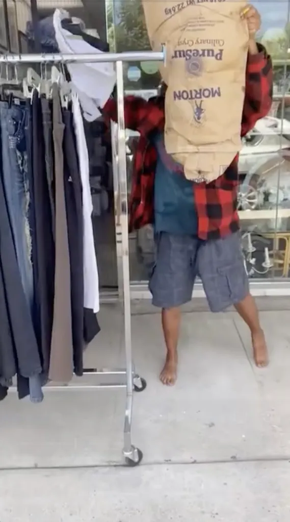 A barefoot man wearing a red-and-black plaid shirt holds a large Morton salt bag overhead outside a store in Nithya Raman's district in Sherman Oaks, California.