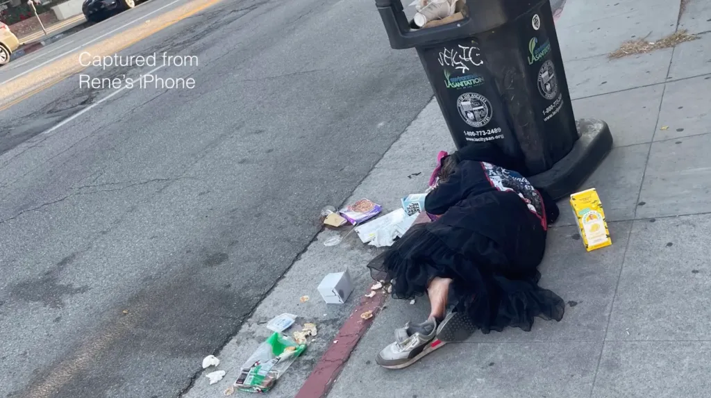A person lying on the sidewalk in Sherman Oaks, California, next to a trash can and scattered debris.