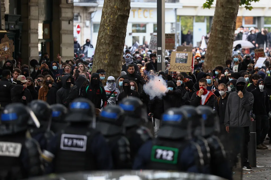 Anti-criminality police in riot gear face a large crowd of demonstrators holding signs and a firecracker during a cost of living protest in Lille, France.