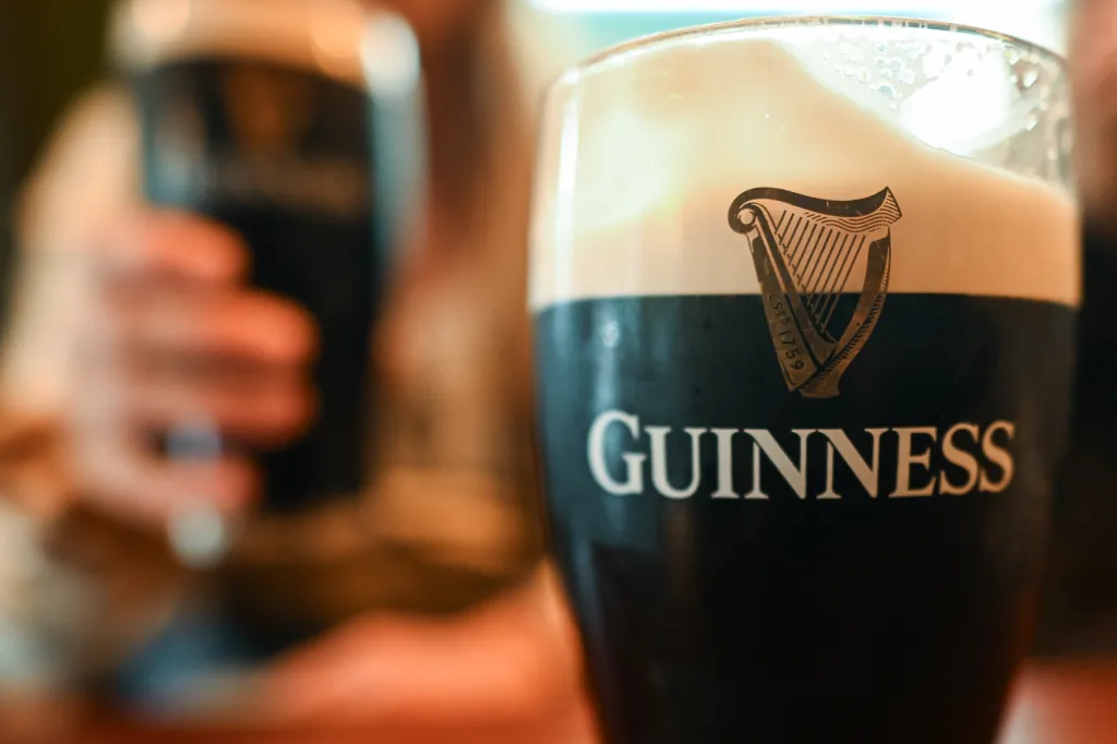 A freshly poured pint of Guinness stout sits on a dark wooden table inside a local pub in Dublin, Ireland.