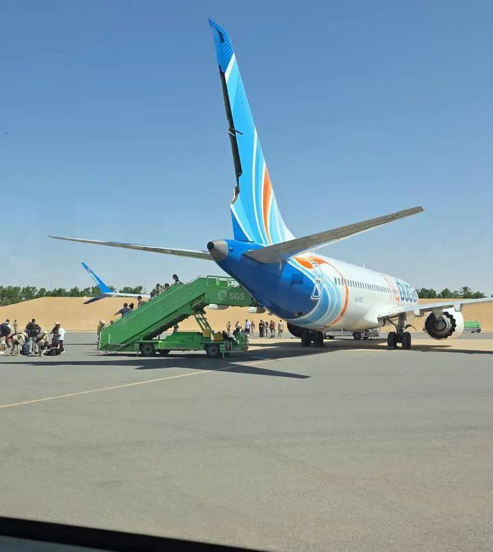 A Flydubai Boeing 737 Max 8 plane on the tarmac with passengers boarding via stairs.