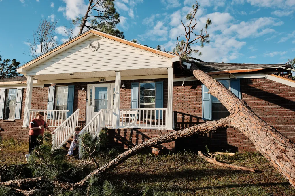 Gabriel Johnson and Mikaila Sullivan sitting outside their storm-damaged home with a tree fallen through the roof.
