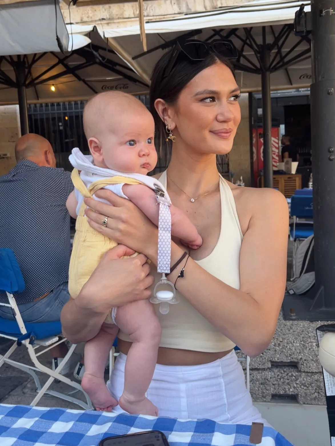 A woman holding a baby while sitting at an outdoor cafe.