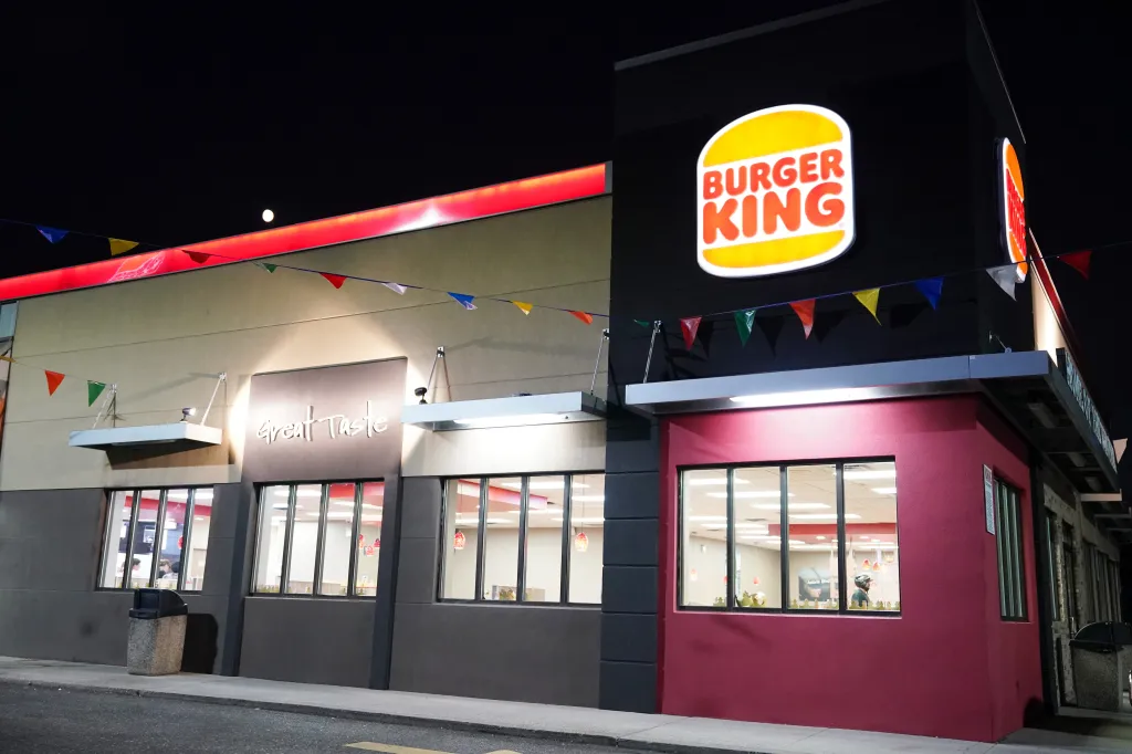 Exterior view of a Burger King restaurant at night, with illuminated signage and colorful pennant flags.