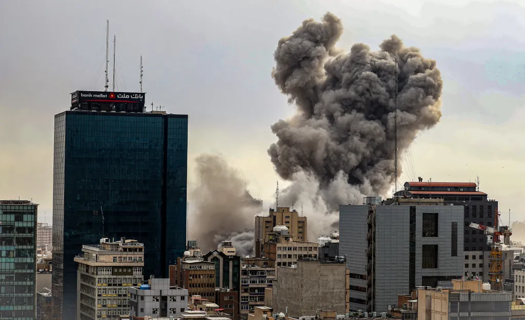 Thick smoke rises behind city buildings in Tehran, Iran, following reported explosions.