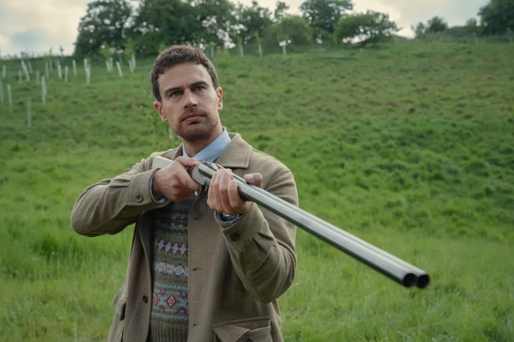 Theo James aiming a shotgun in an outdoor setting in a scene from The Gentlemen.