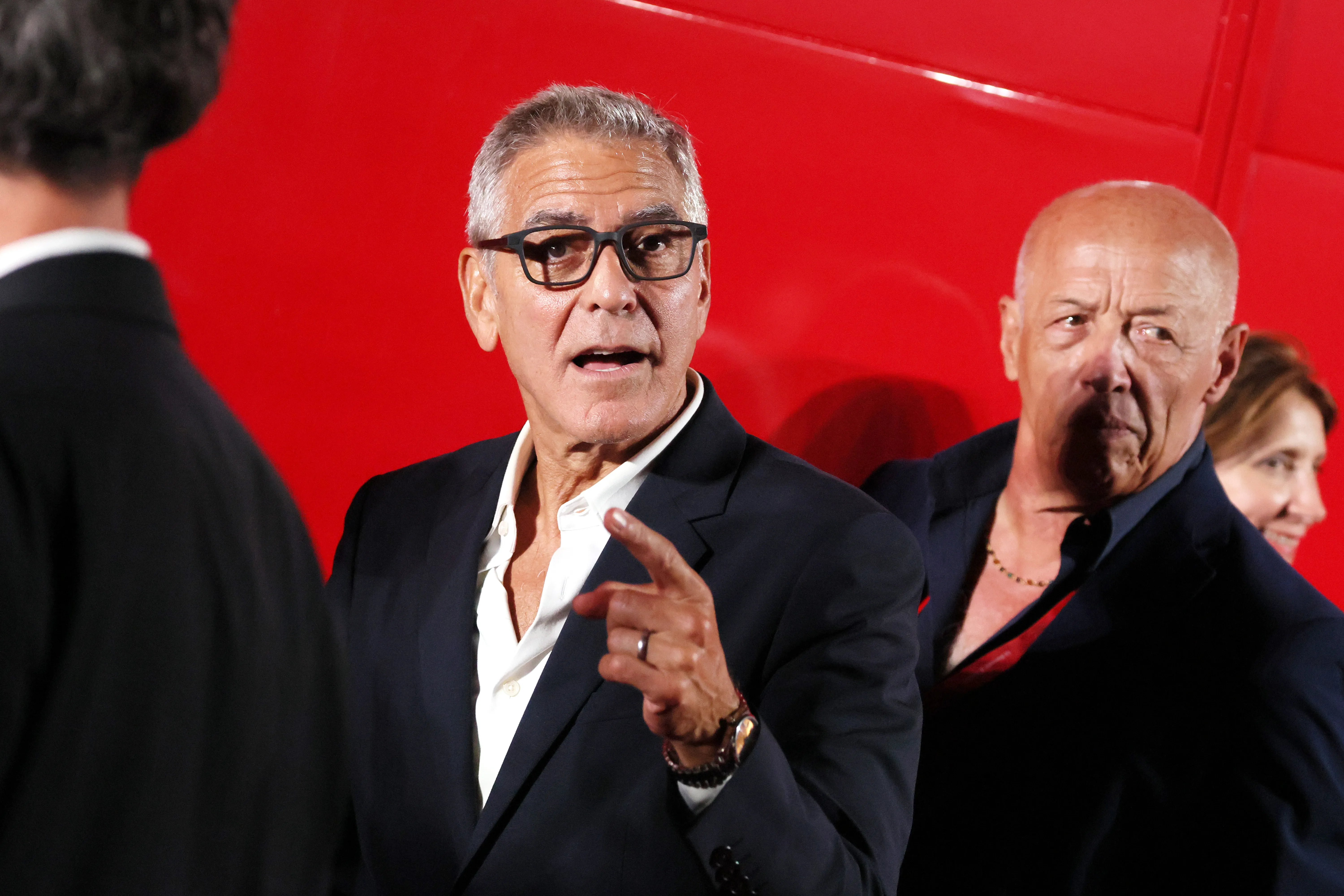 George Clooney wearing glasses and pointing his finger at a screening event.