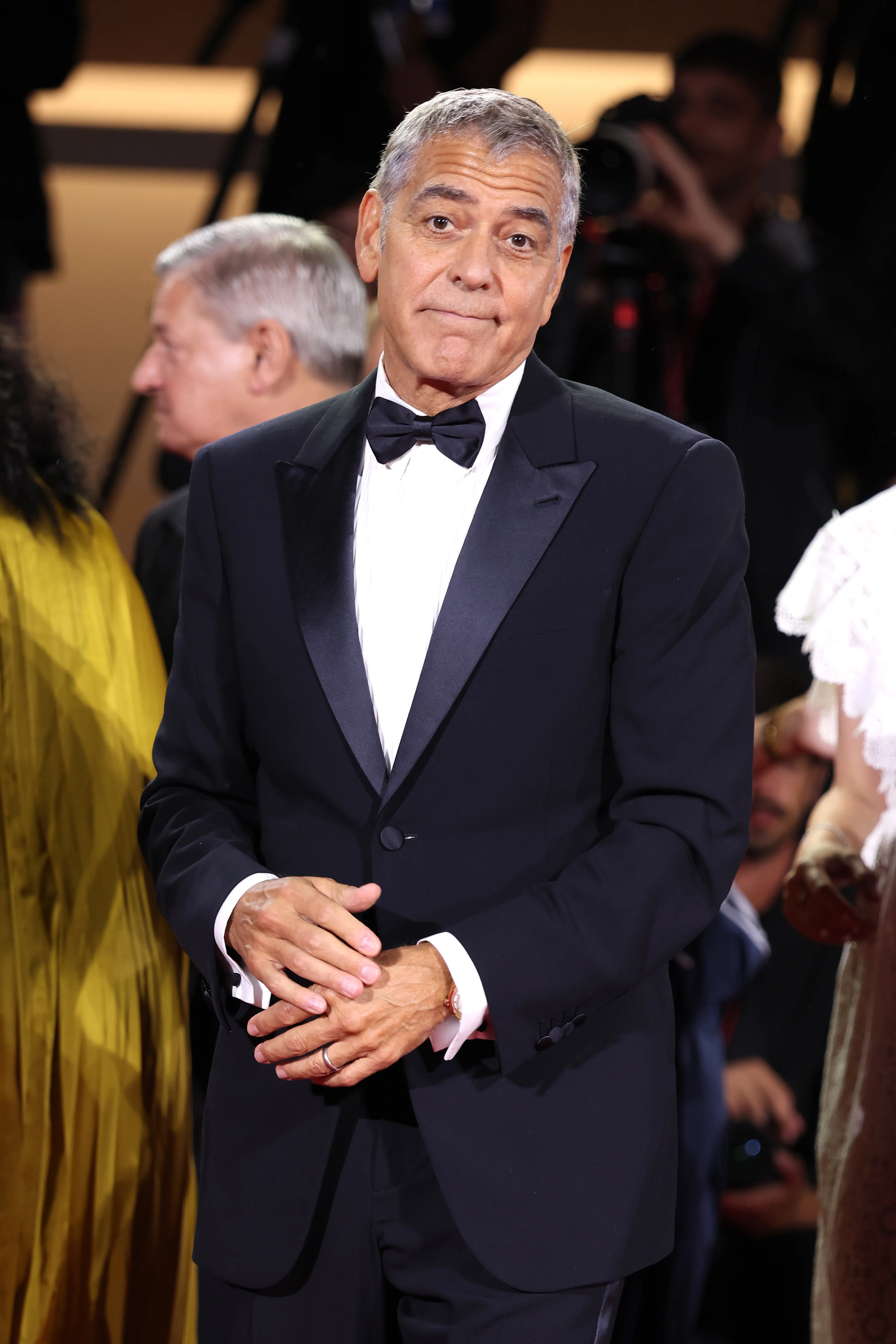 George Clooney on the red carpet at the Venice International Film Festival, wearing a tuxedo with a bow tie.