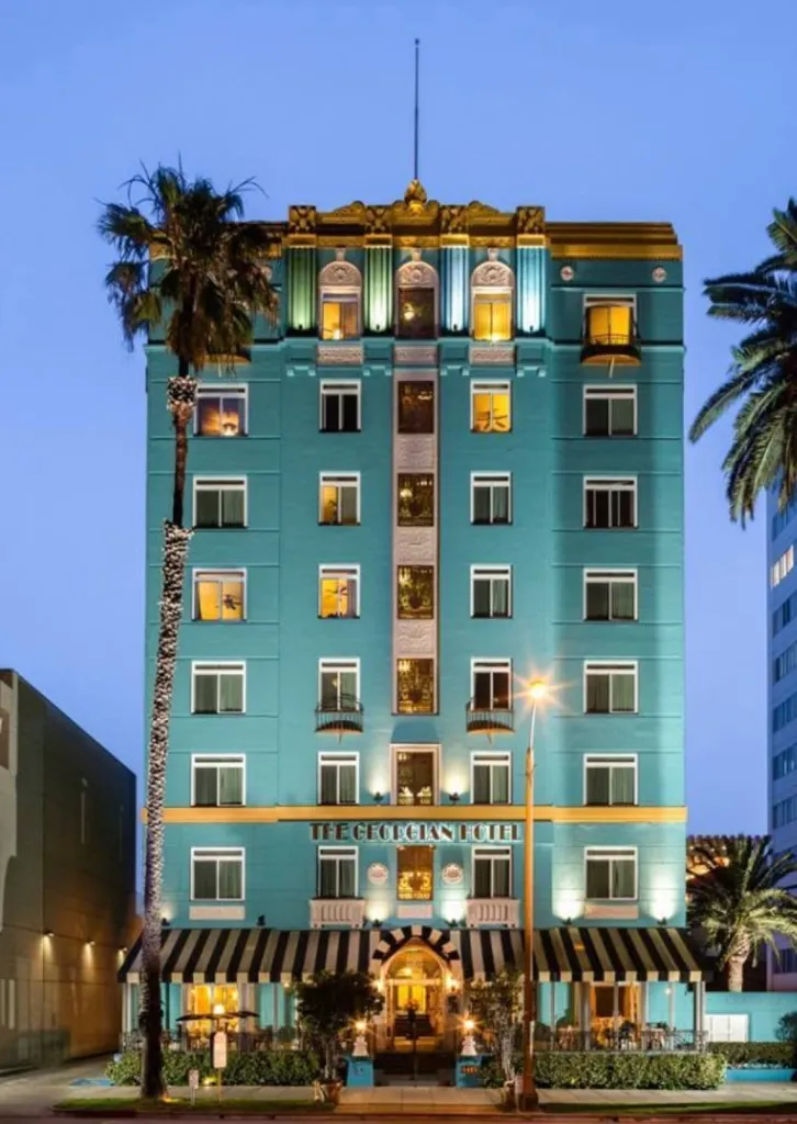 The Georgian Hotel exterior at dusk, featuring its teal facade, striped awnings, and surrounding palm trees.