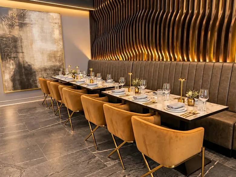 Interior of the Il Vero restaurant, featuring tables set with white plates and gold cutlery, surrounded by gold-velvet armchairs and tufted leather banquette seating.