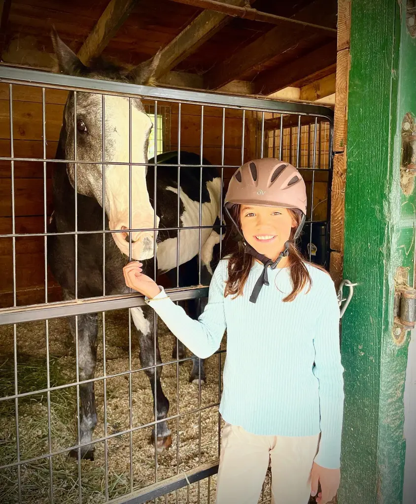 Chad Lowe's daughter Fiona Lowe wearing a riding helmet while standing next to a horse in a stable.