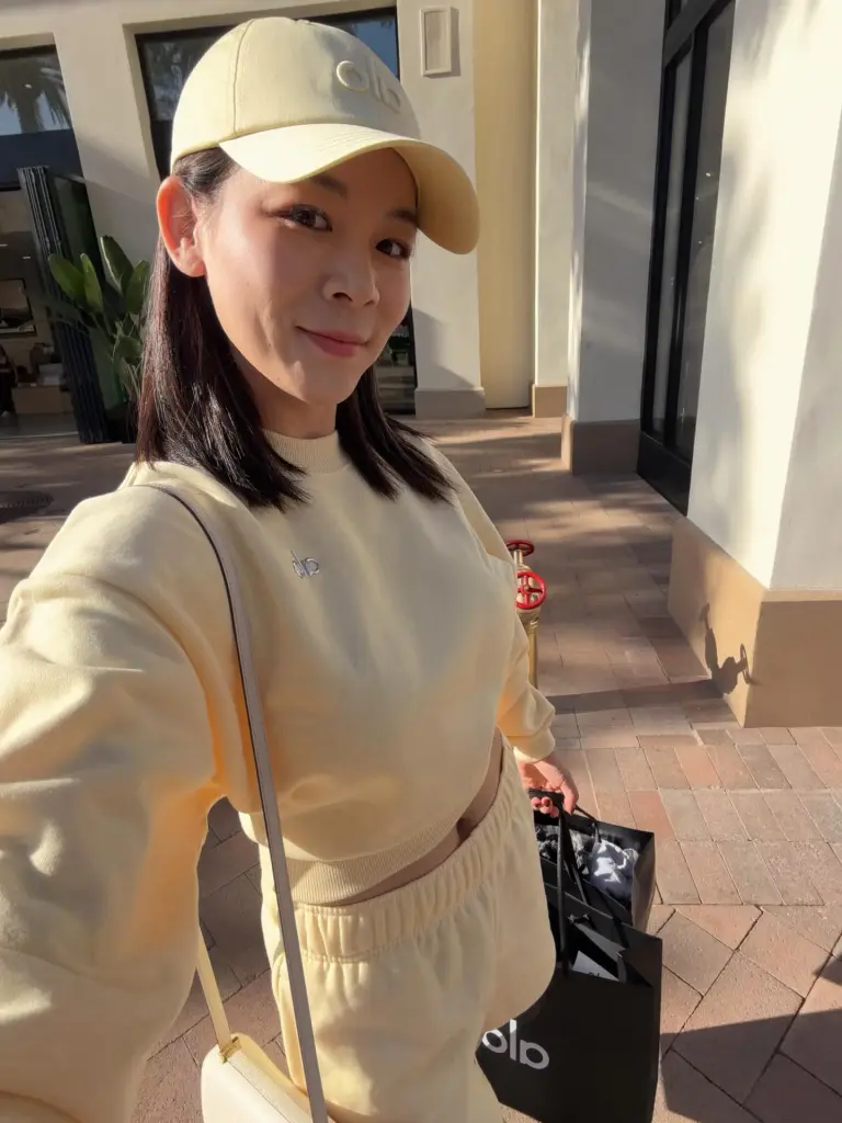 Wanying Zhang, also known as Heather Zhang, wearing a yellow outfit and cap while holding shopping bags.