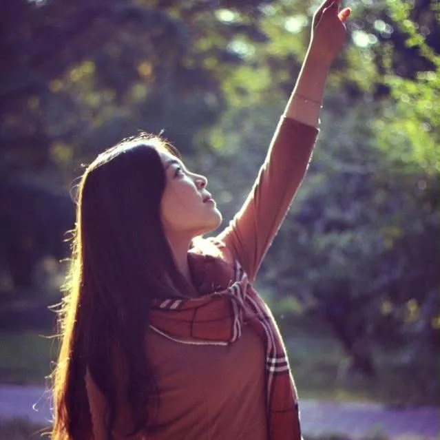 Wanying Zhang raises her hand while standing outdoors among trees.