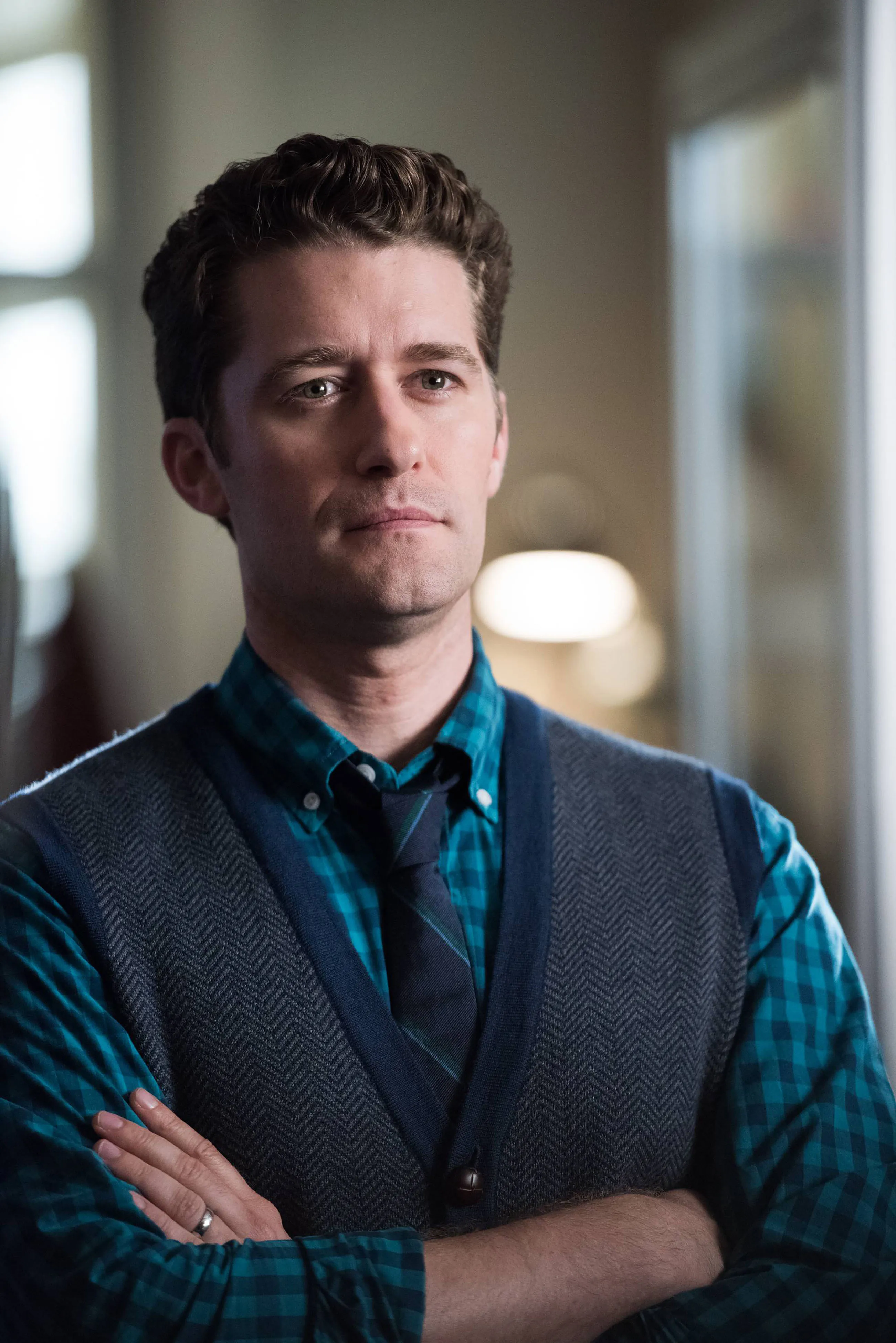 Portrait of Matthew Morrison with arms folded, wearing a plaid shirt, necktie, and vest.