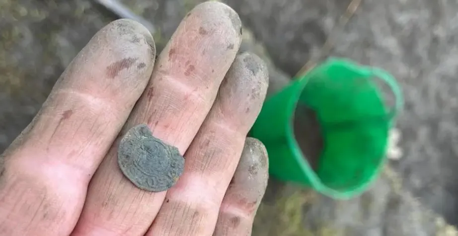 A person's dirt-covered fingers hold a 1,000-year-old Anglo-Saxon gold coin linked to King Ethelred the Unready.