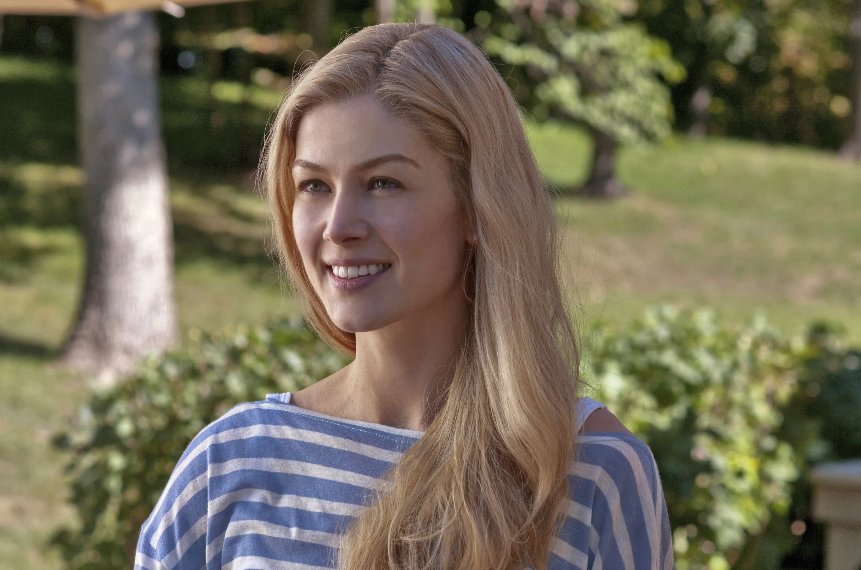 Rosamund Pike smiling outdoors in a blue and white striped top.