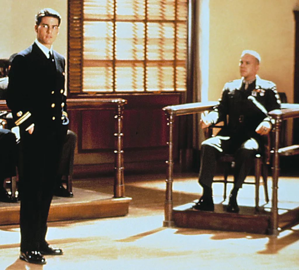 Film still of Tom Cruise standing and Kiefer Sutherland sitting in uniform in a courtroom.