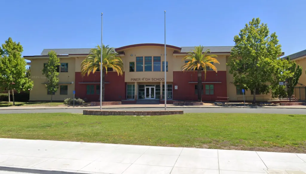 Front view of Piner High School building with palm trees and a lawn in front under a clear sky.