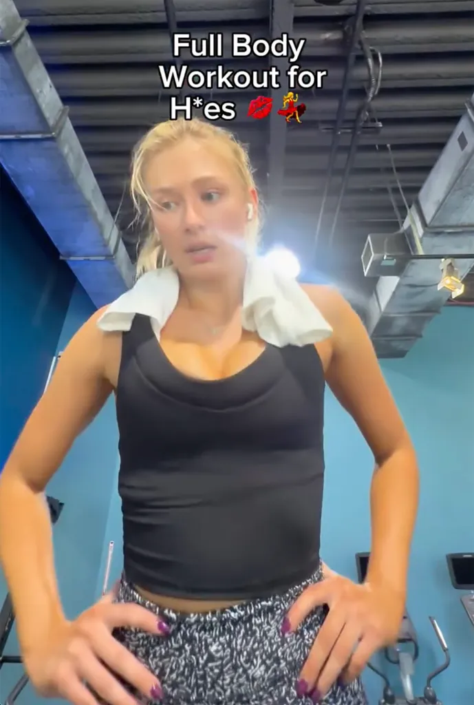 A woman with blonde hair and a white towel around her neck wearing a black tank top and patterned pants stands in a gym, with the text 