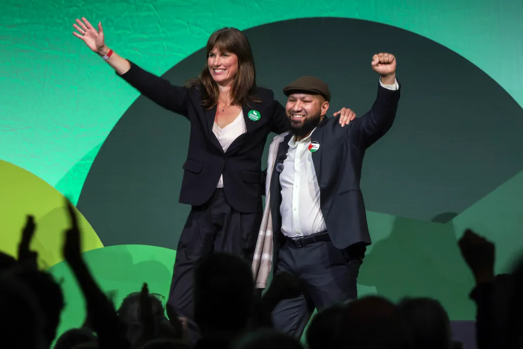Two Green Party members stand on a stage waving to the audience during their conference at the Brighton Centre.