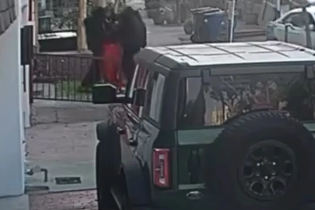 Security camera footage showing a dark SUV parked on a street while an altercation or robbery occurs in the background.