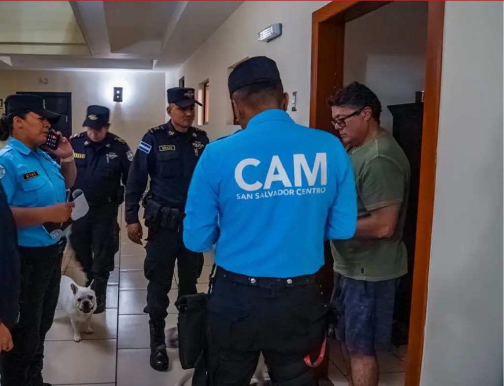 Héctor Alejandro Rosales Bonilla being detained by police officers in a hallway.
