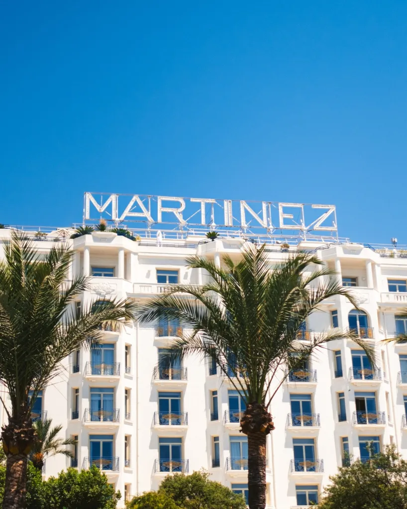 Hôtel Martinez in Cannes with palm trees against a clear blue sky.