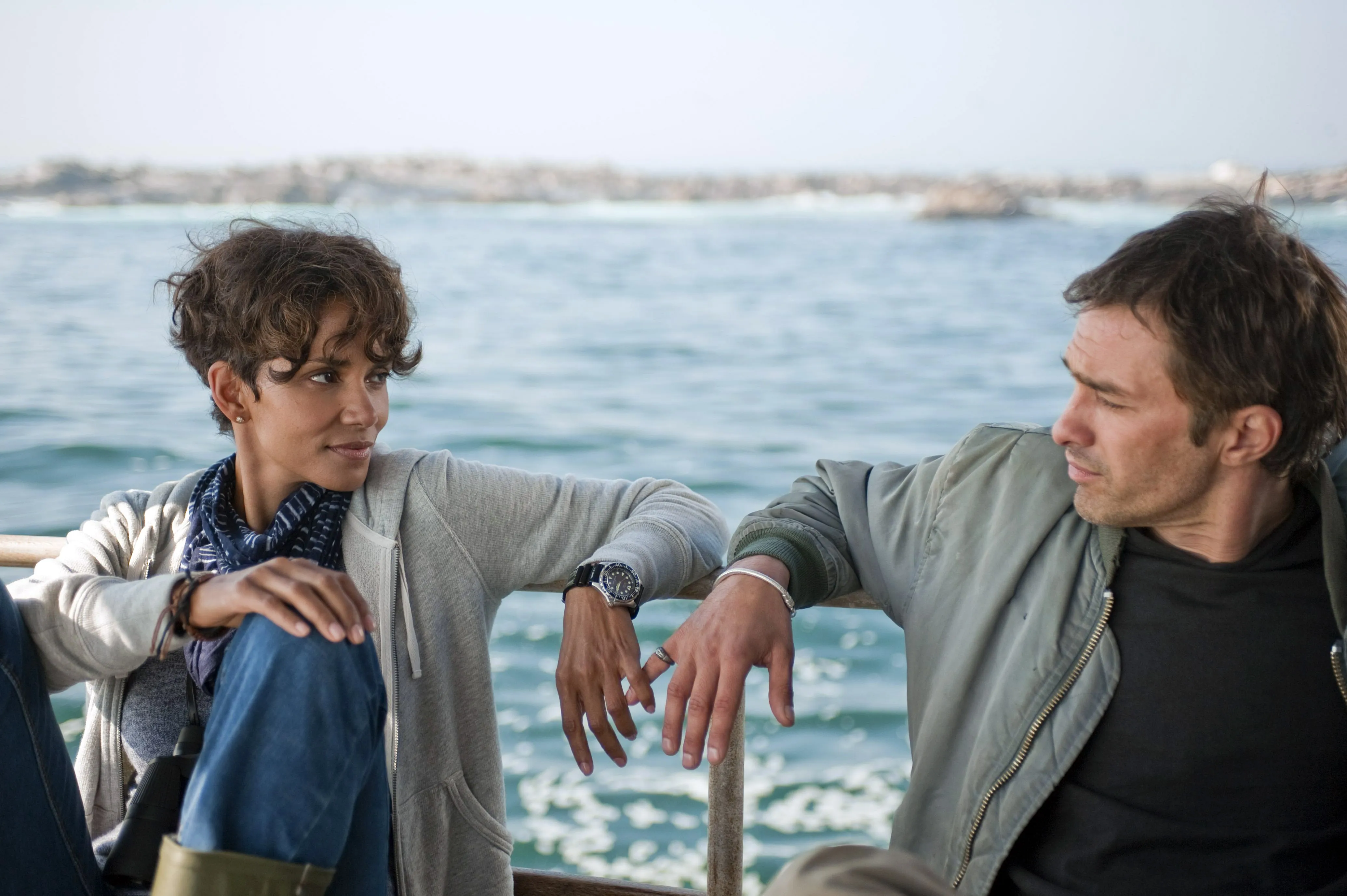 Halle Berry and Olivier Martinez face each other while leaning against a railing on a boat in the film Dark Tide.