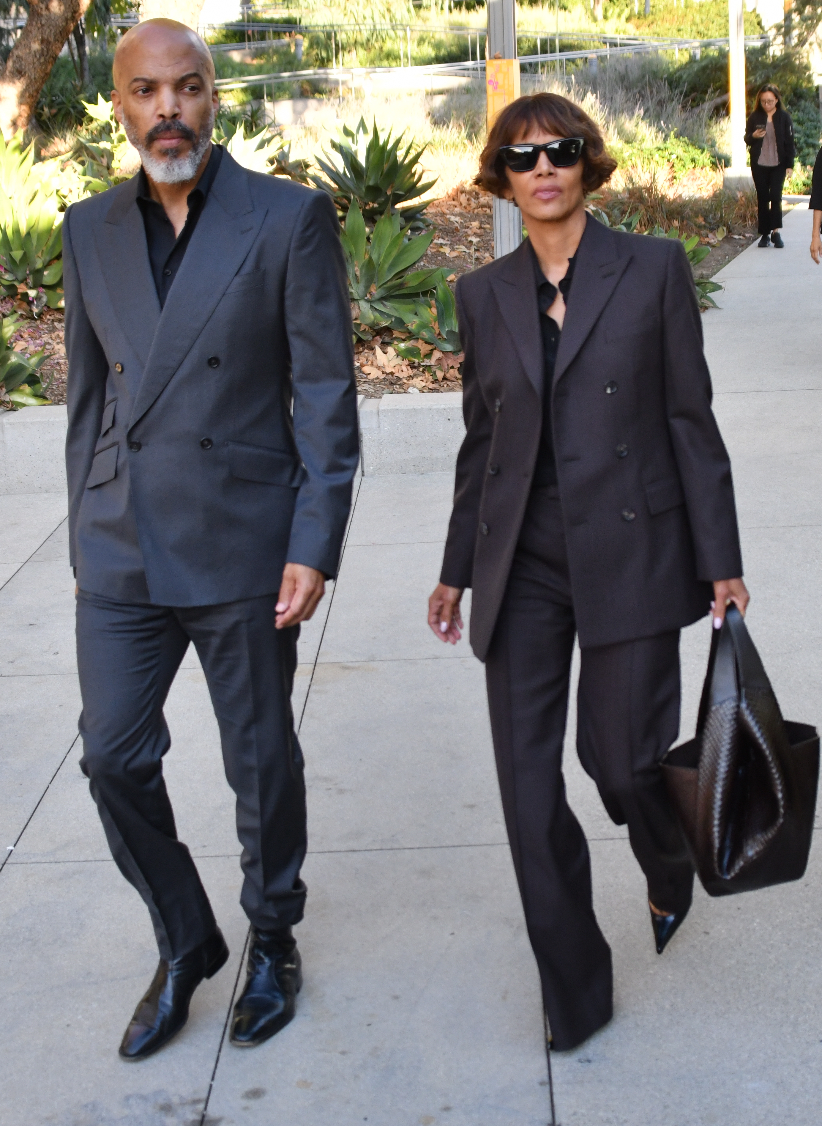 Halle Berry and Van Hunt walking together outdoors, both wearing matching dark suits.
