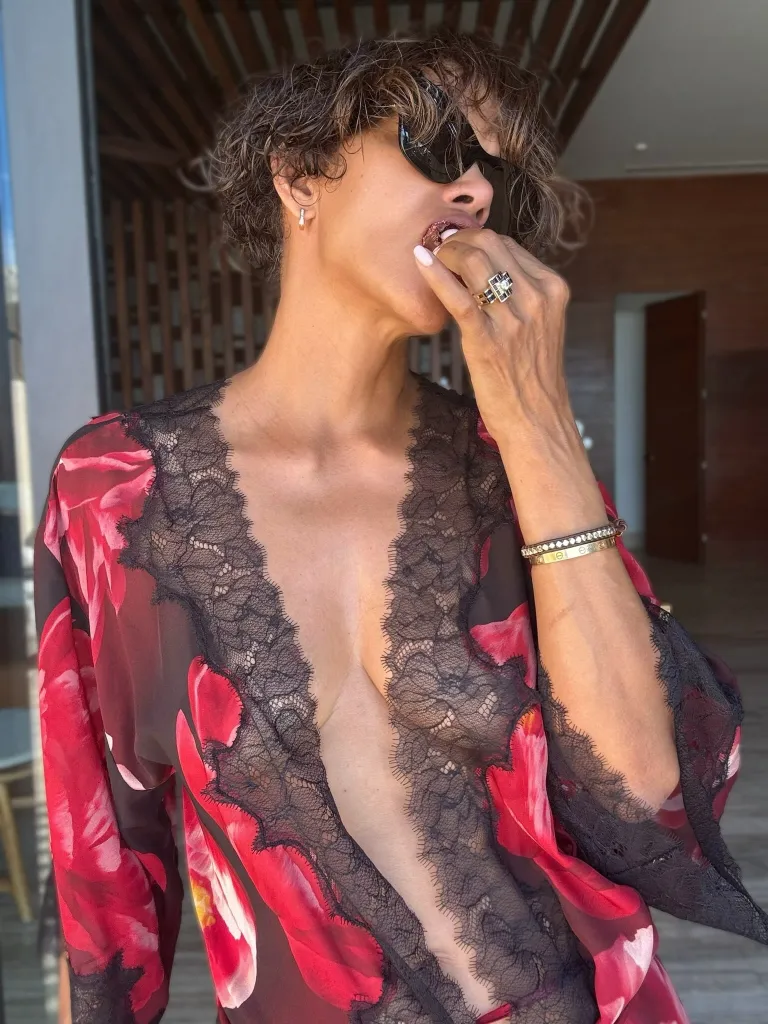 Halle Berry wearing sunglasses and a red floral robe with black lace, eating something.