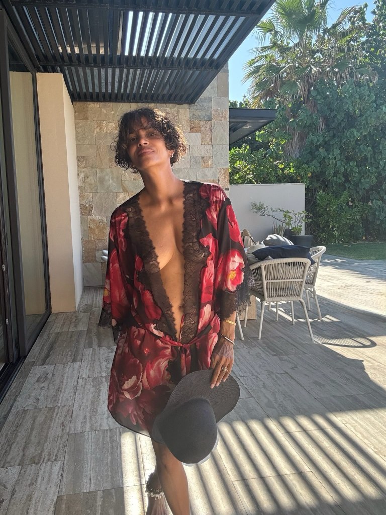 Halle Berry celebrating her birthday on an outdoor patio while wearing a floral robe and holding a black hat.