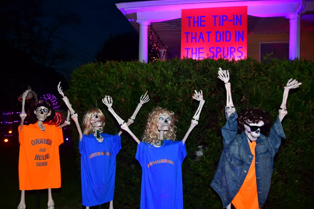 A Halloween lawn display features four skeletons dressed in Knicks-themed gear beneath a sign that reads, 