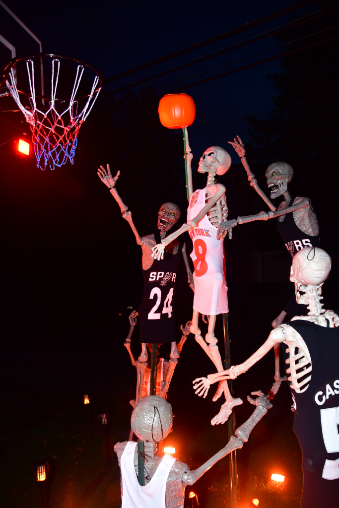 A Halloween display features skeletons recreating an iconic Knicks basketball moment with a pumpkin used as the basketball.
