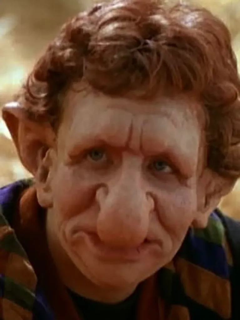 Close-up of a character with heavy prosthetic makeup, featuring large pointed ears, a bulbous nose, and heavy wrinkles, from Halloweentown.