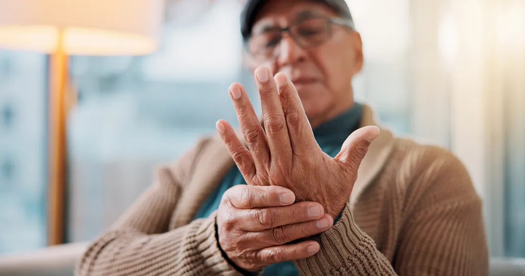 An elderly man holds his hand, experiencing pain and stiffness in his fingers and wrist.